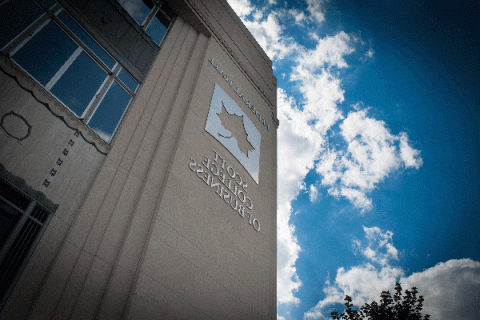 Exterior of a large building with a metallic Sycamore leaf logo and a sign reading “Federal Hall” above the logo and “Scott College of Business” below the logo with blue sky and clouds. 